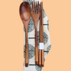 Set of wooden cutlery including a spoon, fork, and chopsticks on a patterned cloth with a beige background.