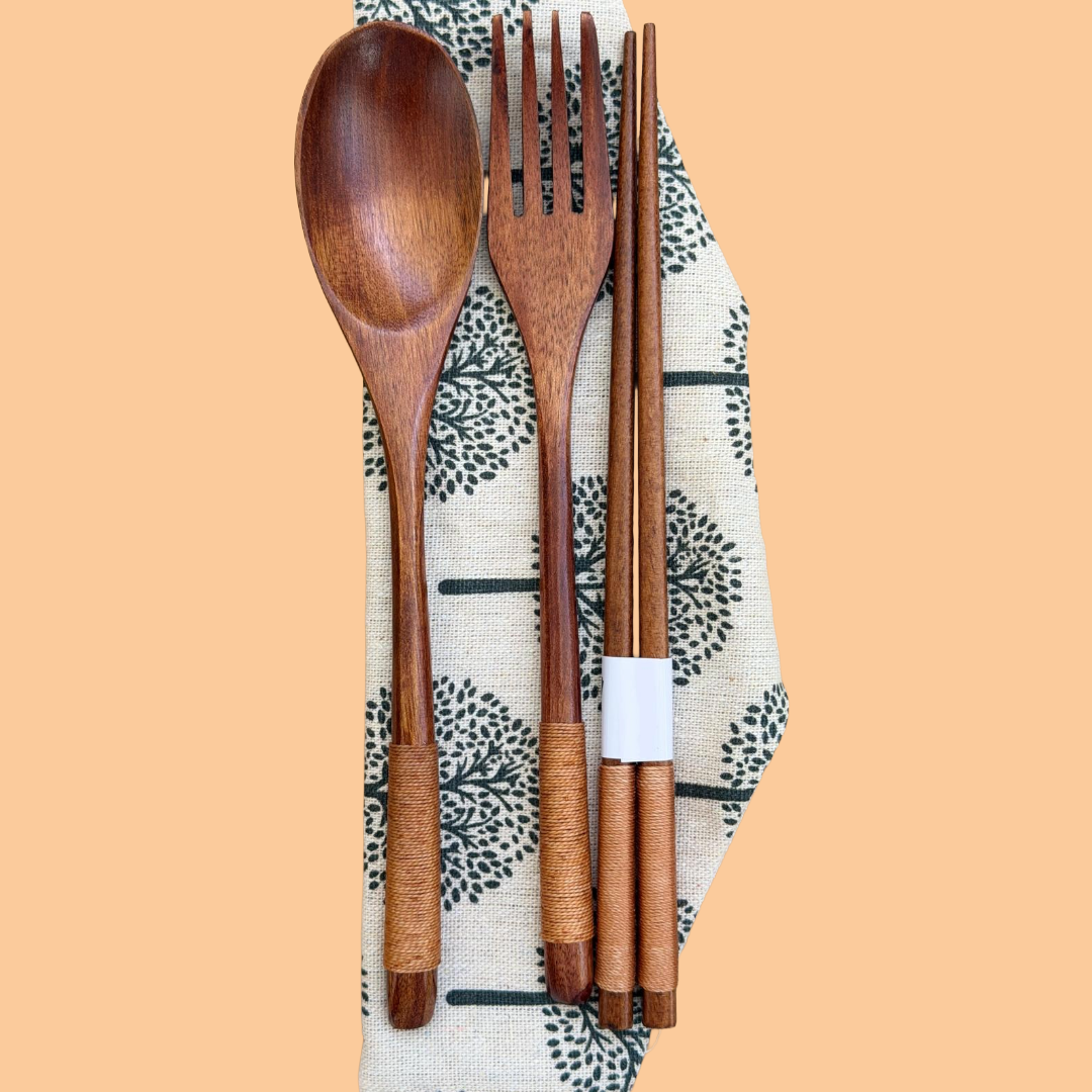 Set of wooden cutlery including a spoon, fork, and chopsticks on a patterned cloth with a beige background.